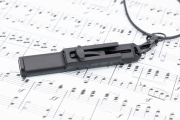 Vocal Trainer lying on printed sheet music with the necklace clip visible.